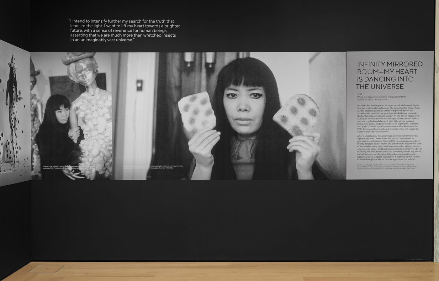 Installation view of One with Eternity: Yayoi Kusama at the Buffalo AKG Art Museum,featuring black-and-white images of Kusama and wall text set on aluminum